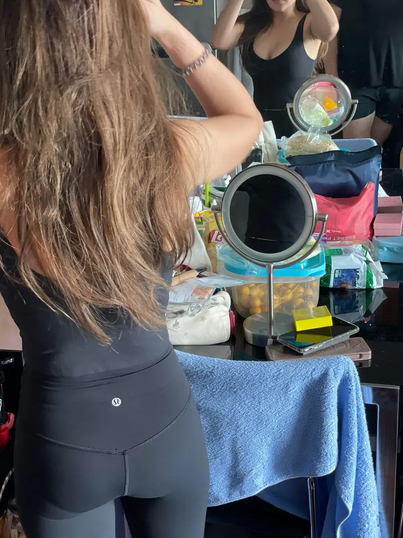 A slender woman with long brown hair wearing black Lululemon leggings and a tank top taking a mirror selfie.