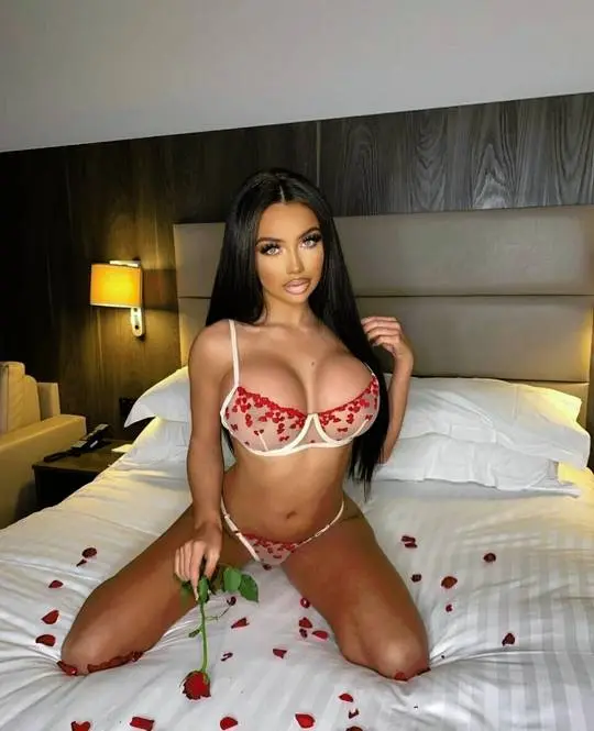 Busty mixed woman in red and white heart-patterned lingerie sitting on a bed with rose petals