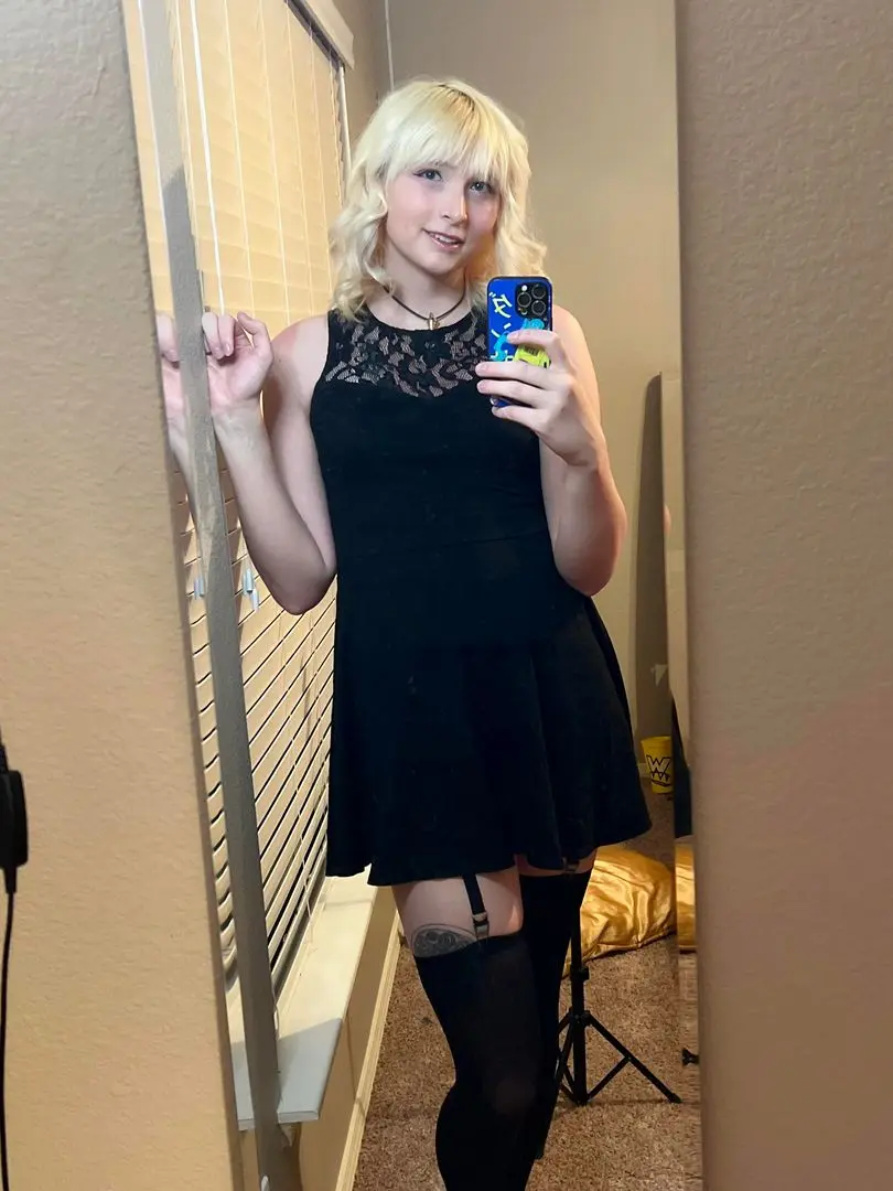 MTF selfie of a blonde woman in a black mini dress and stockings with garters taking a mirror selfie