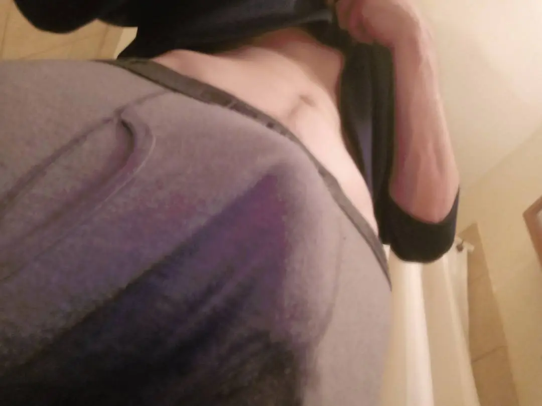 A person with light skin wearing grey sweatpants and a dark shirt lifted to show their stomach.