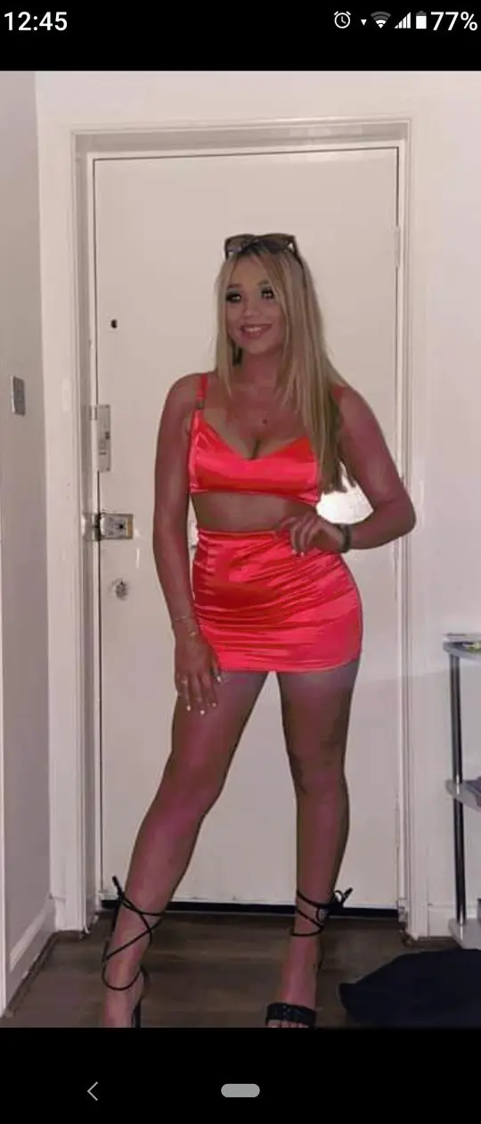 Curvy blonde Glasgow chav girl in a red satin crop top, mini skirt, and black lace-up high heels.