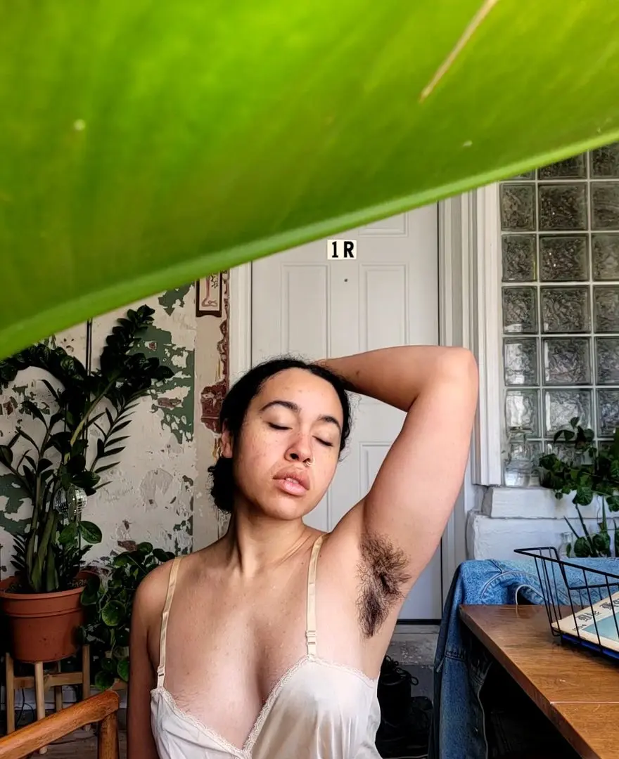 Mixed slim woman with hairy armpits posing in a white camisole outdoors