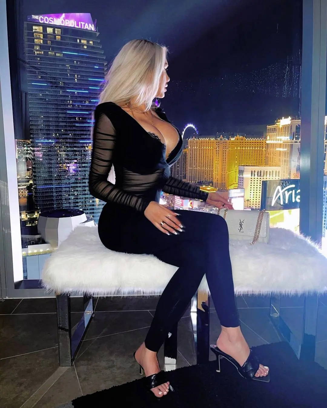 Curvy blonde trophy wife in a black sheer top and high heels on a white faux-fur bench overlooking Las Vegas at night