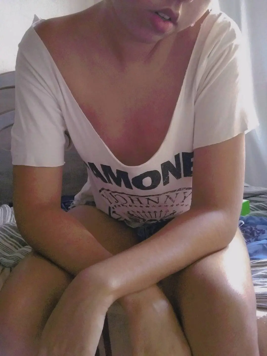Amone Johnny wearing a white v-neck t-shirt sitting on a bed in a casual selfie