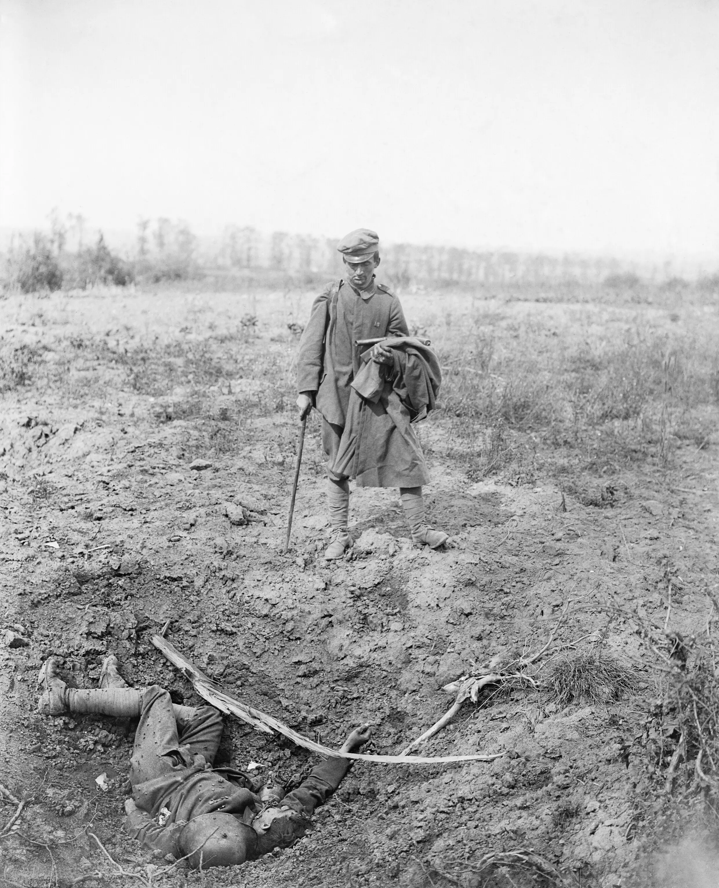 “Capture of Meteren by the 9th (Scottish) Division, 19th July 1918. A captured German prisoner, carrying a Very Light Pistol (flare gun), on his way back (unescorted) looking at a dead comrade lying at the bottom of a shell-hole, 20th July 1918.” By John Warwick Brooke.