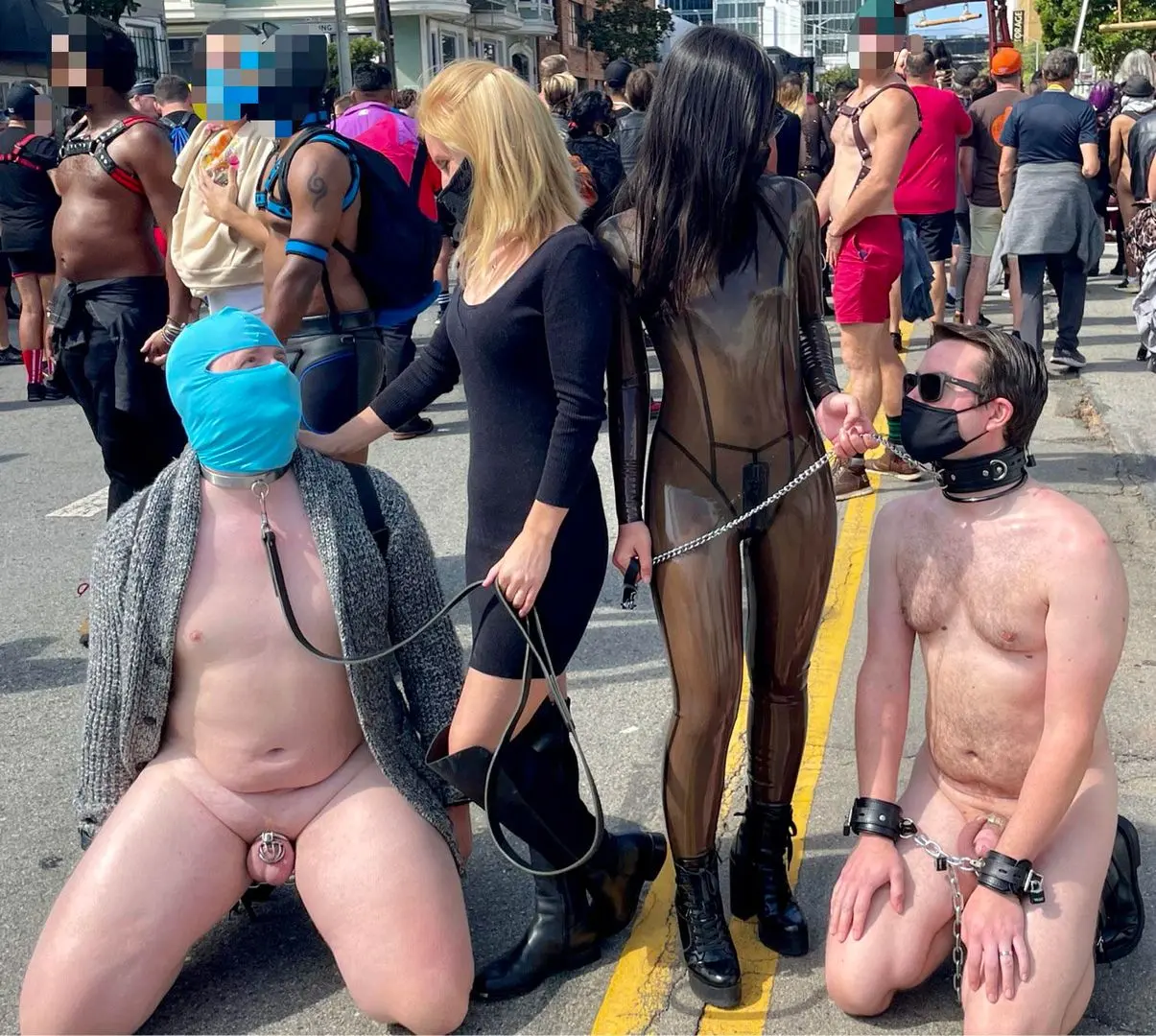 Female dominants leading two naked, handcuffed men on leashes at the Folsom Street Fair.