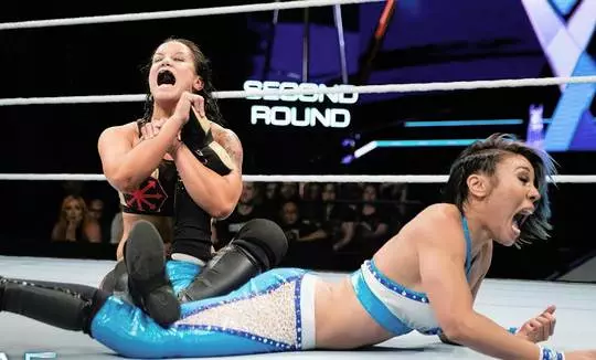 Mia Yim in black and red gear applying an ankle lock submission to another woman in a wrestling ring