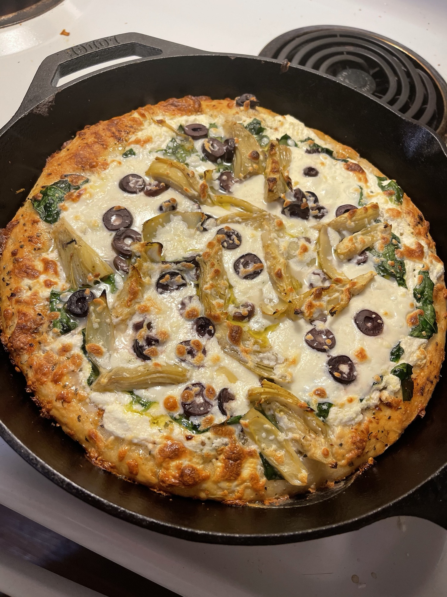 Spinach artichoke pizza with olives, ricotta, mozzarella slices, and feta. Scrolller