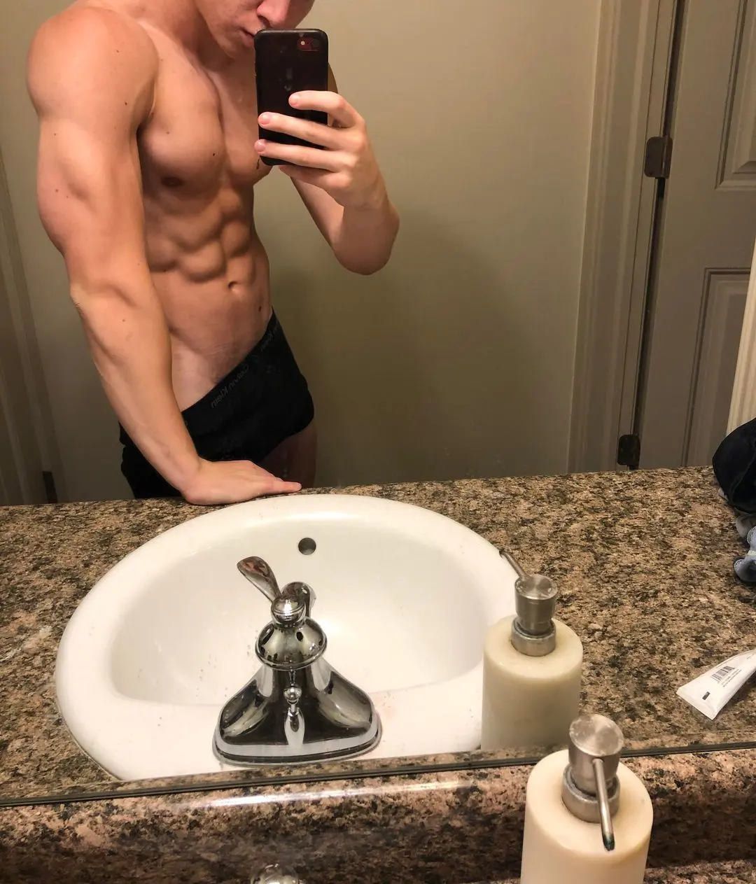 Muscular white twunk flexing in a shirtless mirror selfie wearing black underwear in a bathroom.