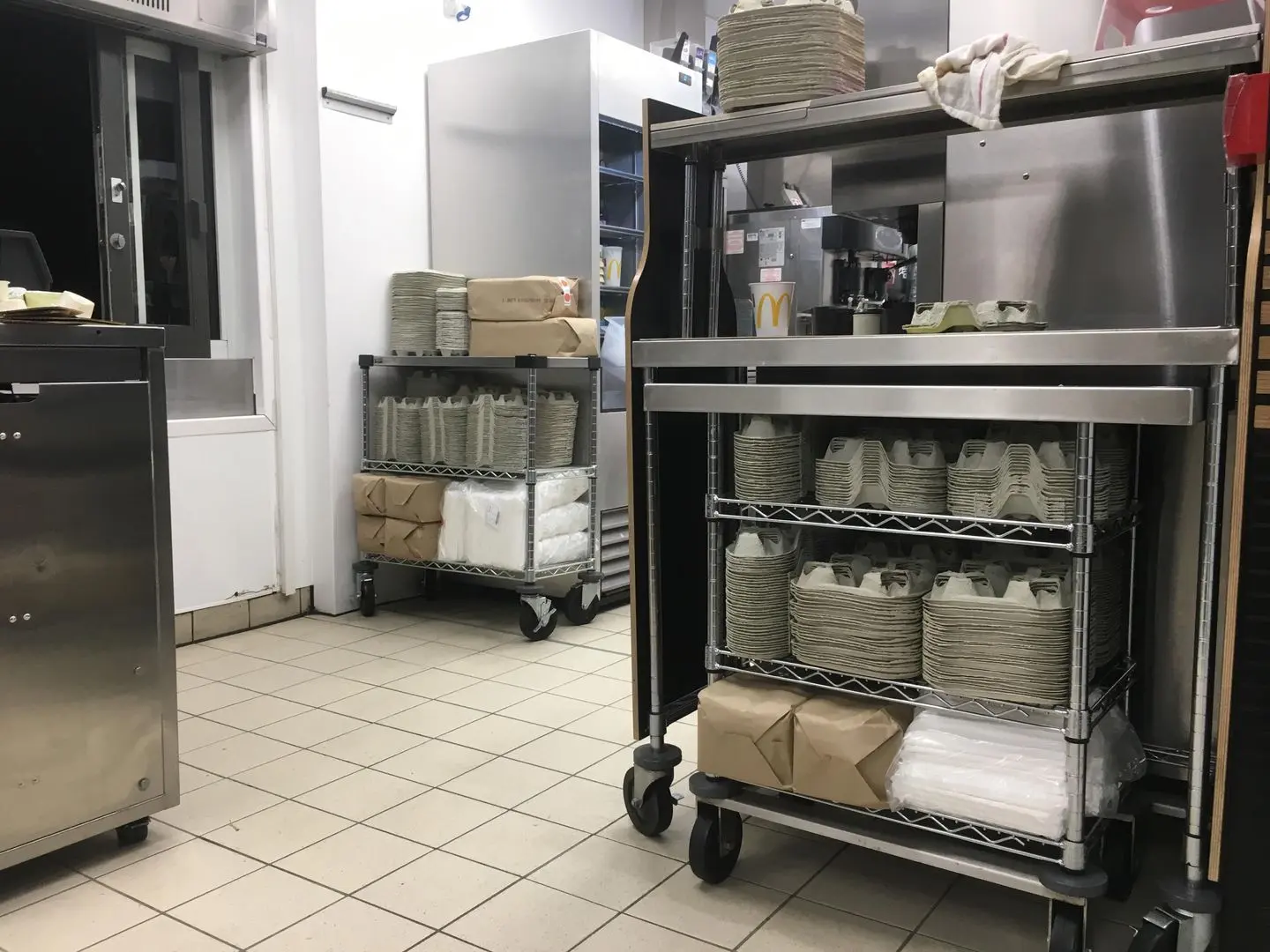 Stainless steel carts stocked with stacks of takeout containers and paper bags in a commercial kitchen