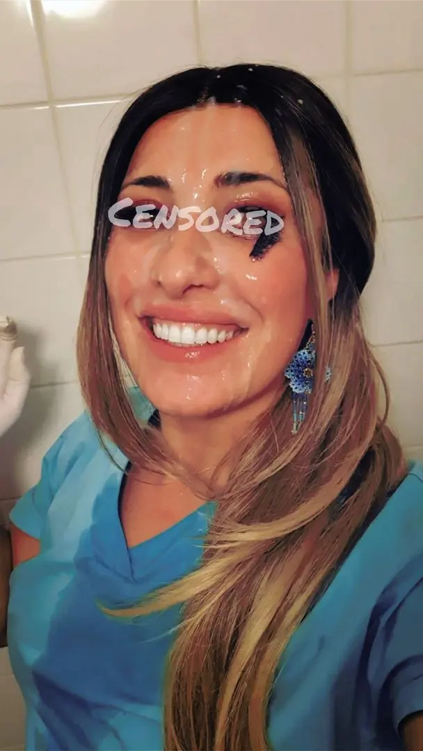 Smiling brunette woman in blue nurse scrubs with a cumshot facial selfie in a bathroom