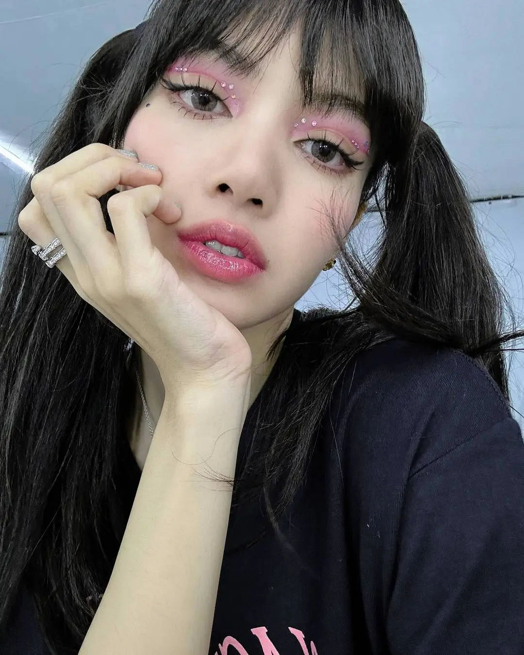 Lisa from Blackpink in a close-up selfie with pigtails, pink glitter eye makeup, and a black t-shirt.