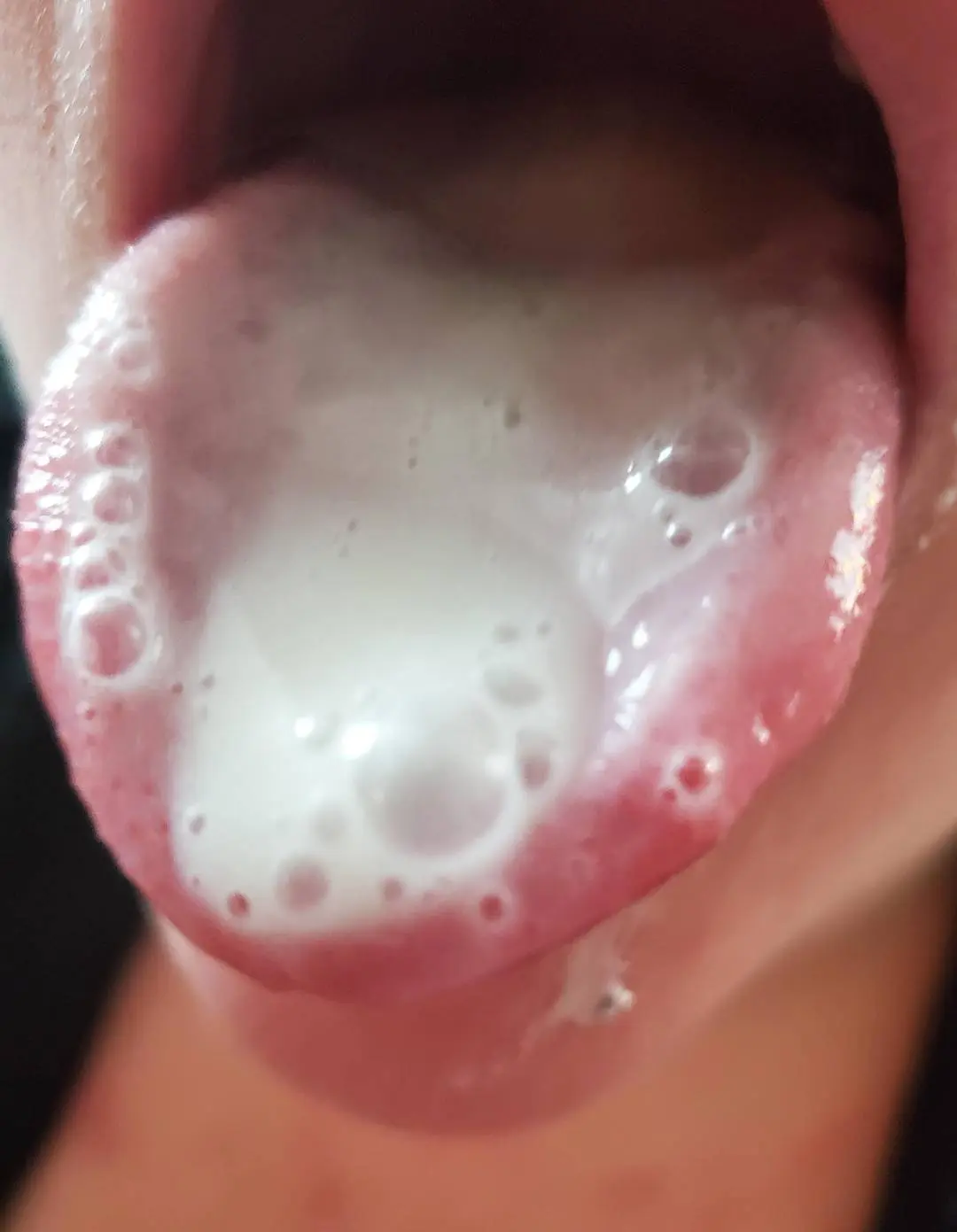 Close-up of a person sticking out their tongue covered in white frothy cum