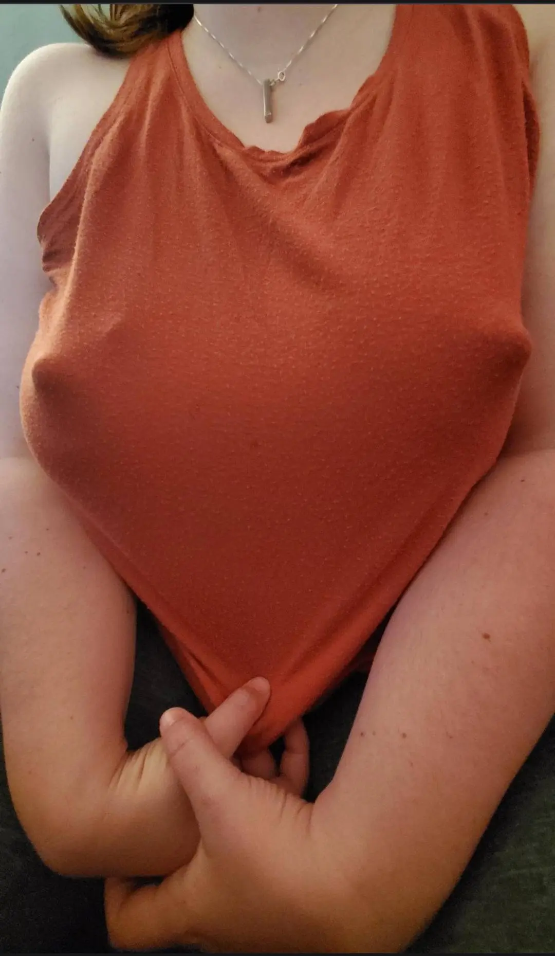 Busty brunette woman in a tight orange tank top with big erect nipples showing through the fabric.