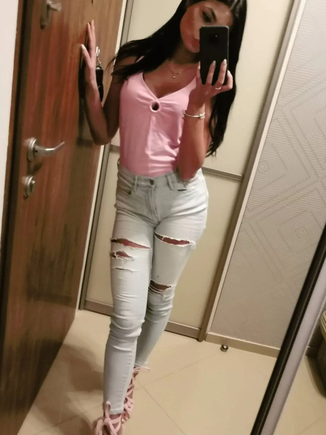 Polish girl taking a mirror selfie in a pink cutout tank top and ripped light-blue skinny jeans