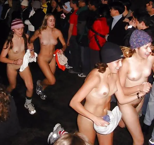 Four slim white college girls in beanies and underwear running topless through a night crowd during a nude college run.