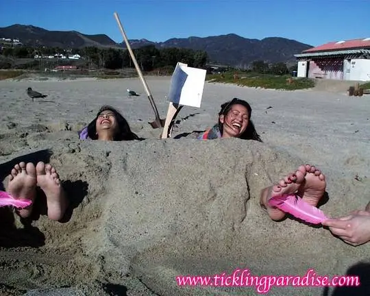 Asian women tickling feet and toes with a pink feather while buried in the sand at the beach