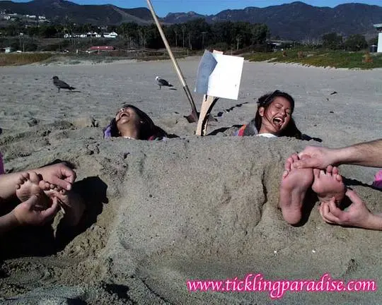 Asian women tickling feet and toes with a pink feather while buried in the sand at the beach