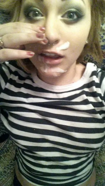 Slim blonde woman with a nose piercing in a striped shirt posing for a cum selfie