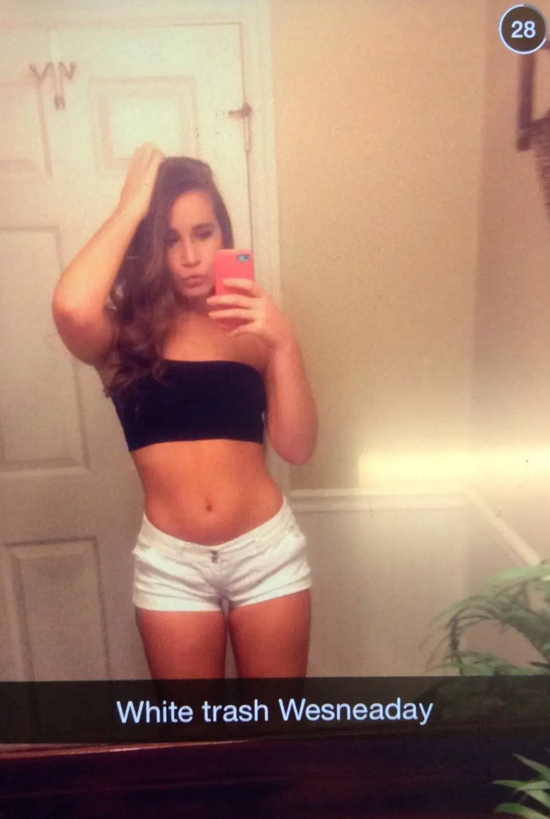 Slim brunette woman in a black tube top and white shorts posing for mirror selfies