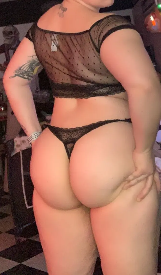 Amputee woman with a thick build posing from behind in a black sheer crop top and lace thong.
