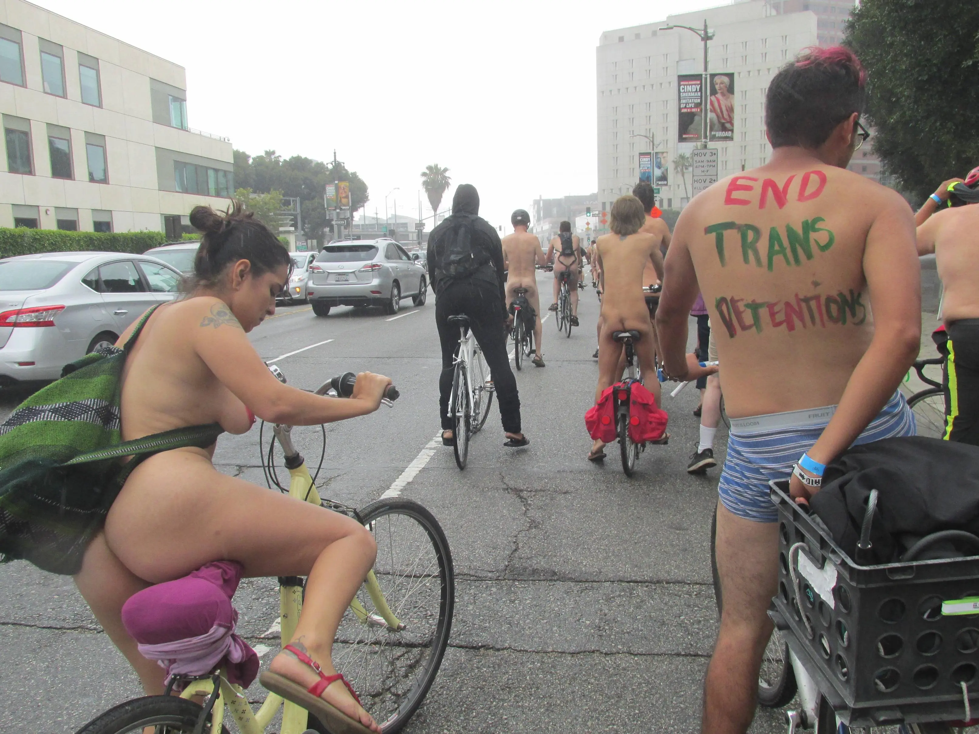 Thick latina with heart pasties and tattoos riding a bicycle at WNBR SF with an interracial group