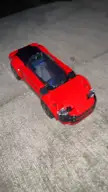 A person's hand manipulating a red LegoCity supercar on a grey fabric surface in a close-up, oddly satisfying clip.