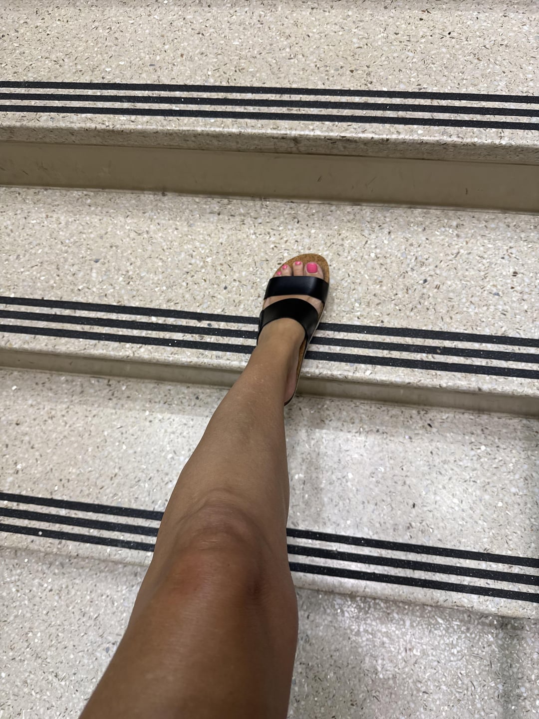 Woman with tanned skin and slim legs wearing black sandals standing on stairs