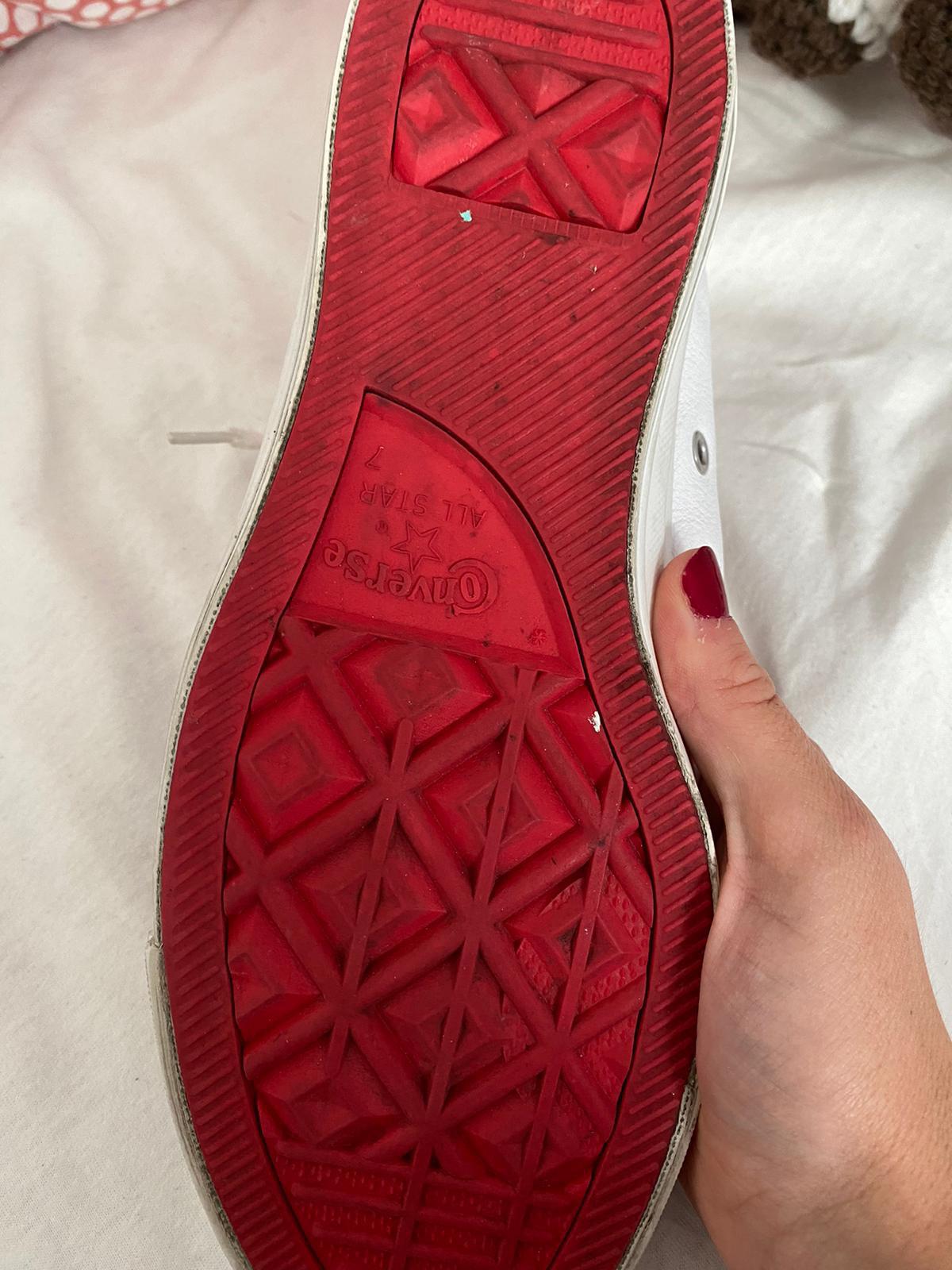 Close-up of a white Converse All Star shoe with a red sole held by a woman's hand