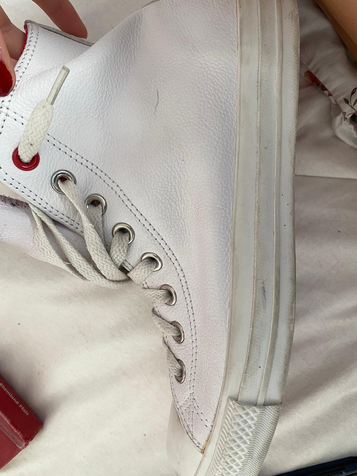 Close-up of a white Converse All Star shoe with a red sole held by a woman's hand
