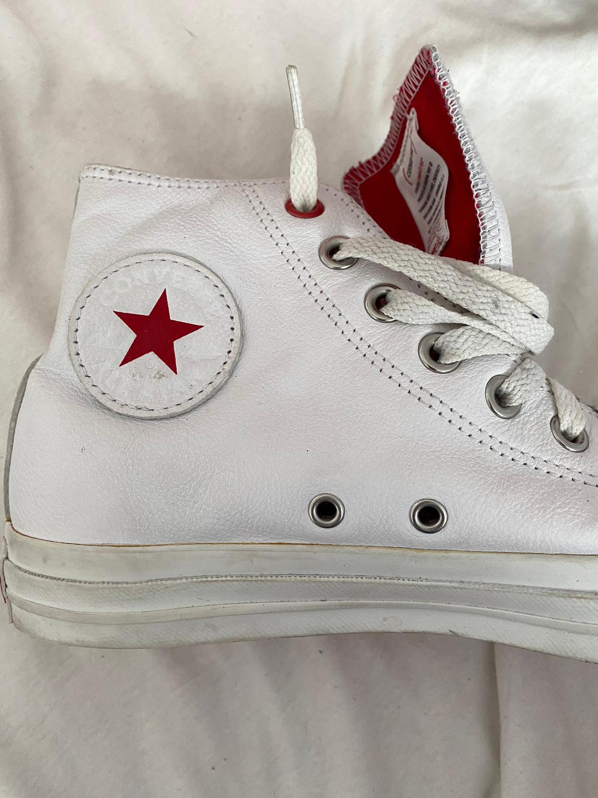 Close-up of a white Converse All Star shoe with a red sole held by a woman's hand