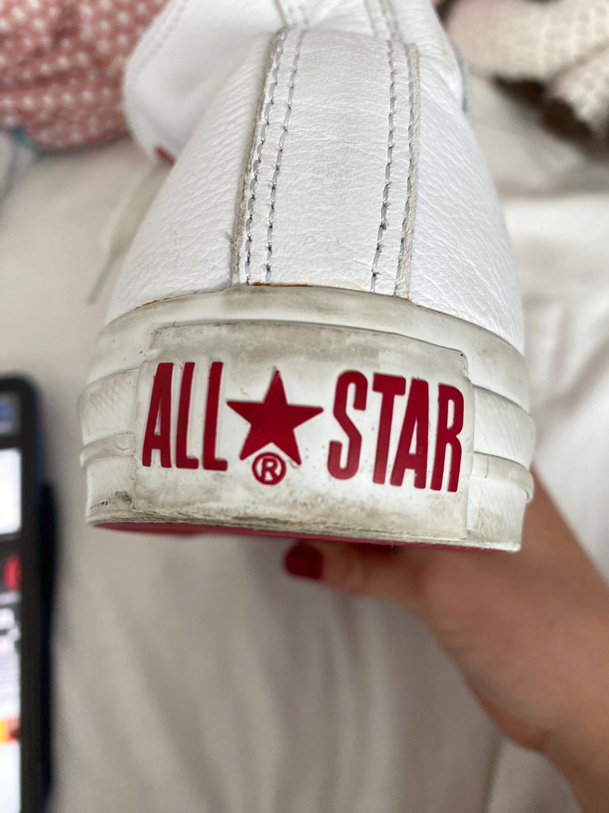 Close-up of a white Converse All Star shoe with a red sole held by a woman's hand