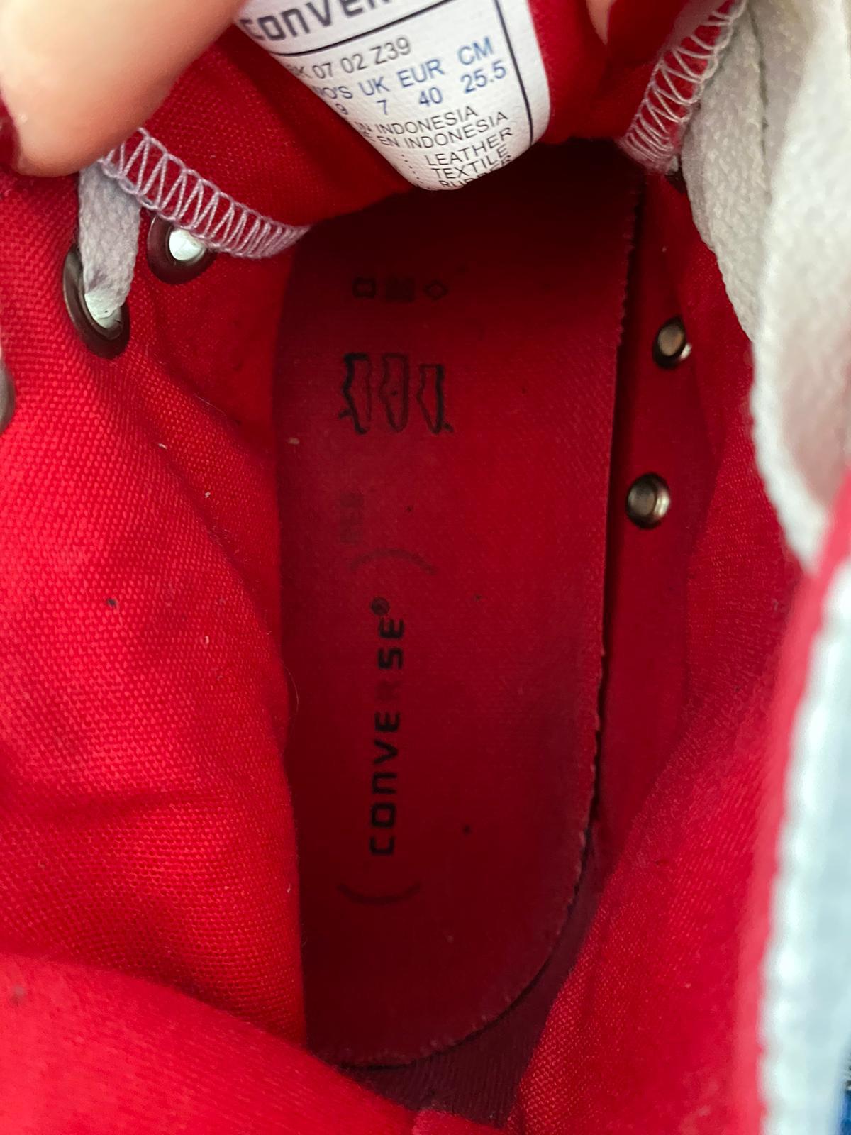Close-up of a white Converse All Star shoe with a red sole held by a woman's hand