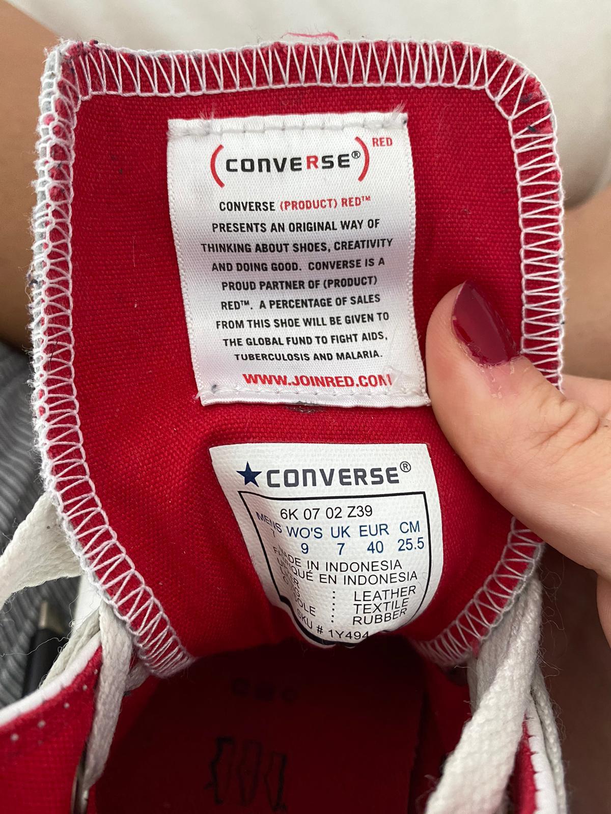 Close-up of a white Converse All Star shoe with a red sole held by a woman's hand