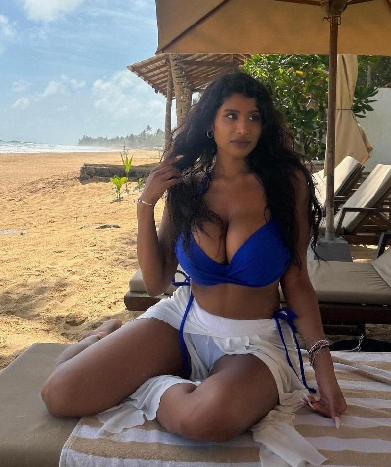 Curvy Sri-Lankan woman with tanned skin and long brunette hair posing in a green bikini and blue bikini on a beach.