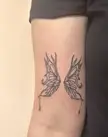 Close-up of a black ink butterfly wings tattoo on a person's upper arm.
