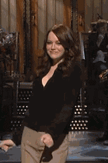 Emma Emma smiling and dancing on a stage in a black long-sleeved top and tan wide-leg pants