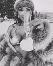 Jeannie Mai in a bikini top, fur coat, and beanie pouring a drink onto snow in a black and white video