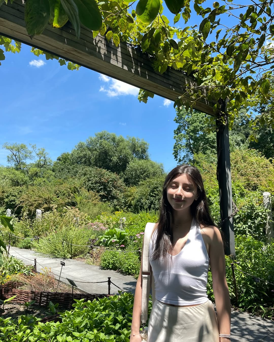 Skye ASMR posing in a sunny garden wearing a white halter top and beige skirt