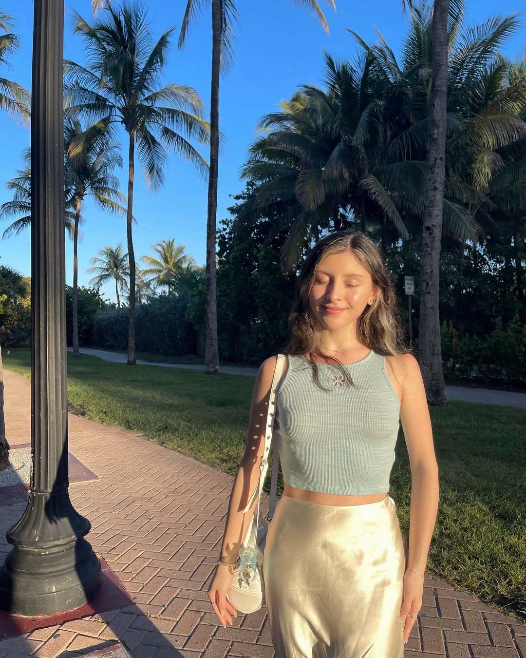 Skye ASMR posing in a sunny garden wearing a white halter top and beige skirt