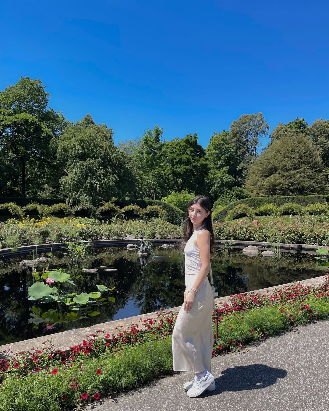 Skye ASMR posing in a sunny garden wearing a white halter top and beige skirt