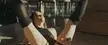 Mikey Madison in Anora wearing a black mesh top and fishnet stockings, lying on her back with legs up