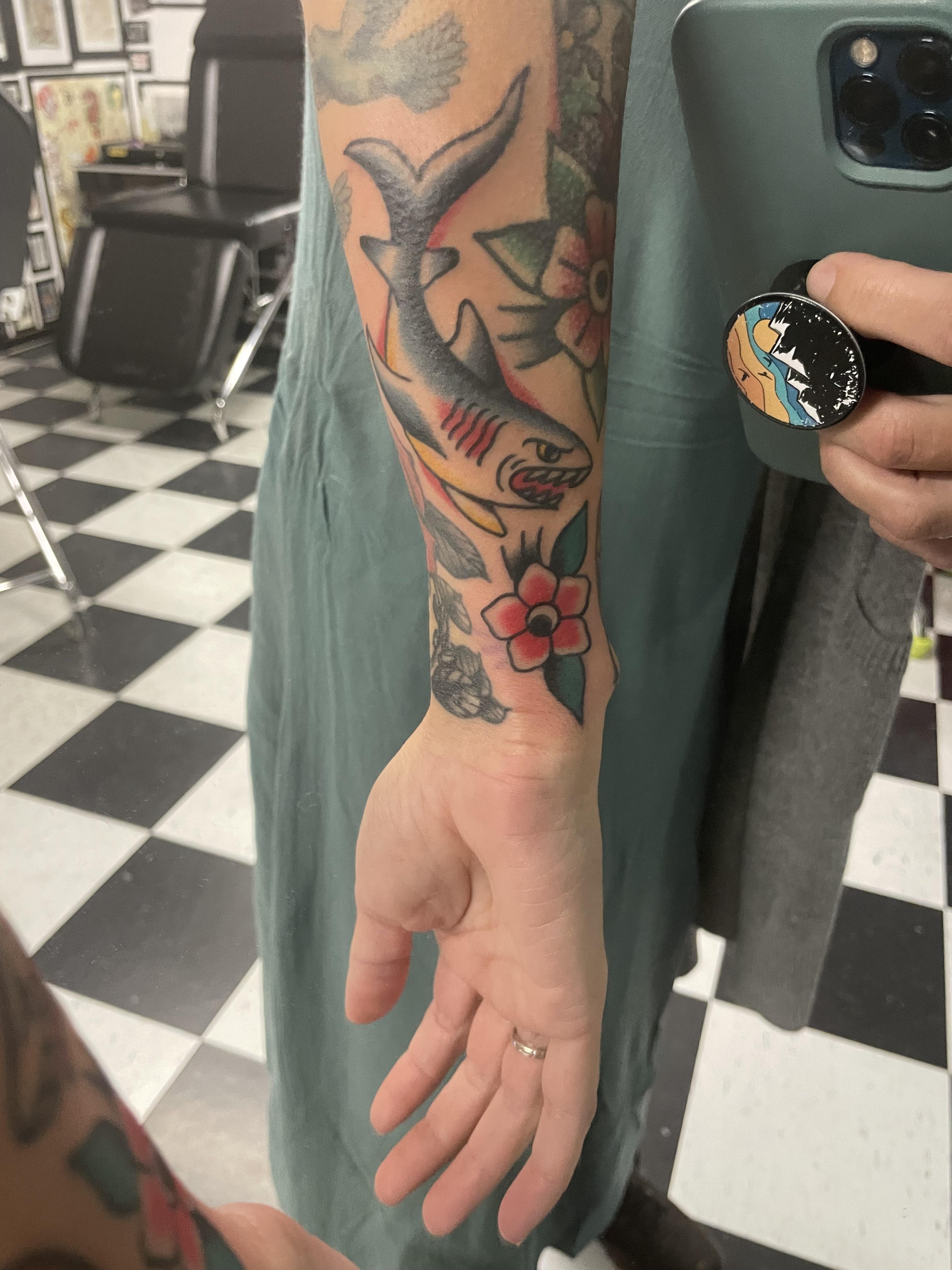 American traditional shark and flower tattoos on a person's forearm