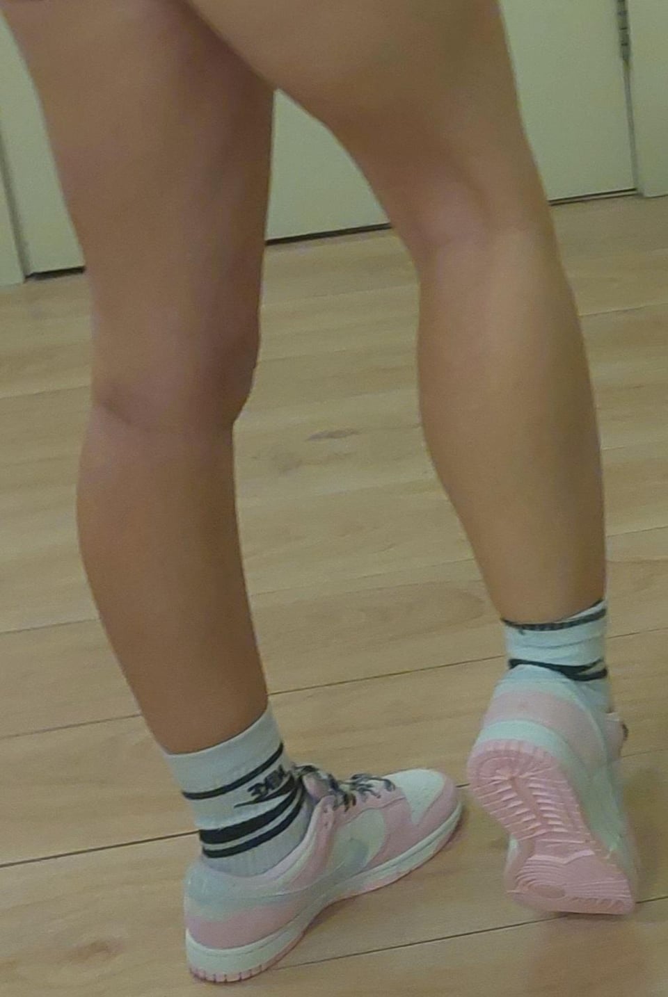 Woman in Nike Dunks and white socks with black stripes standing on a wooden floor