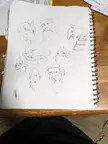 Doodles of scary, weird, and alien monster creature heads in a black and white sketchbook on a wooden table