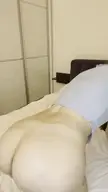 Slim brunette woman on all fours on a bed, showing her bare buttocks and ankle tattoo in a bunny pose.