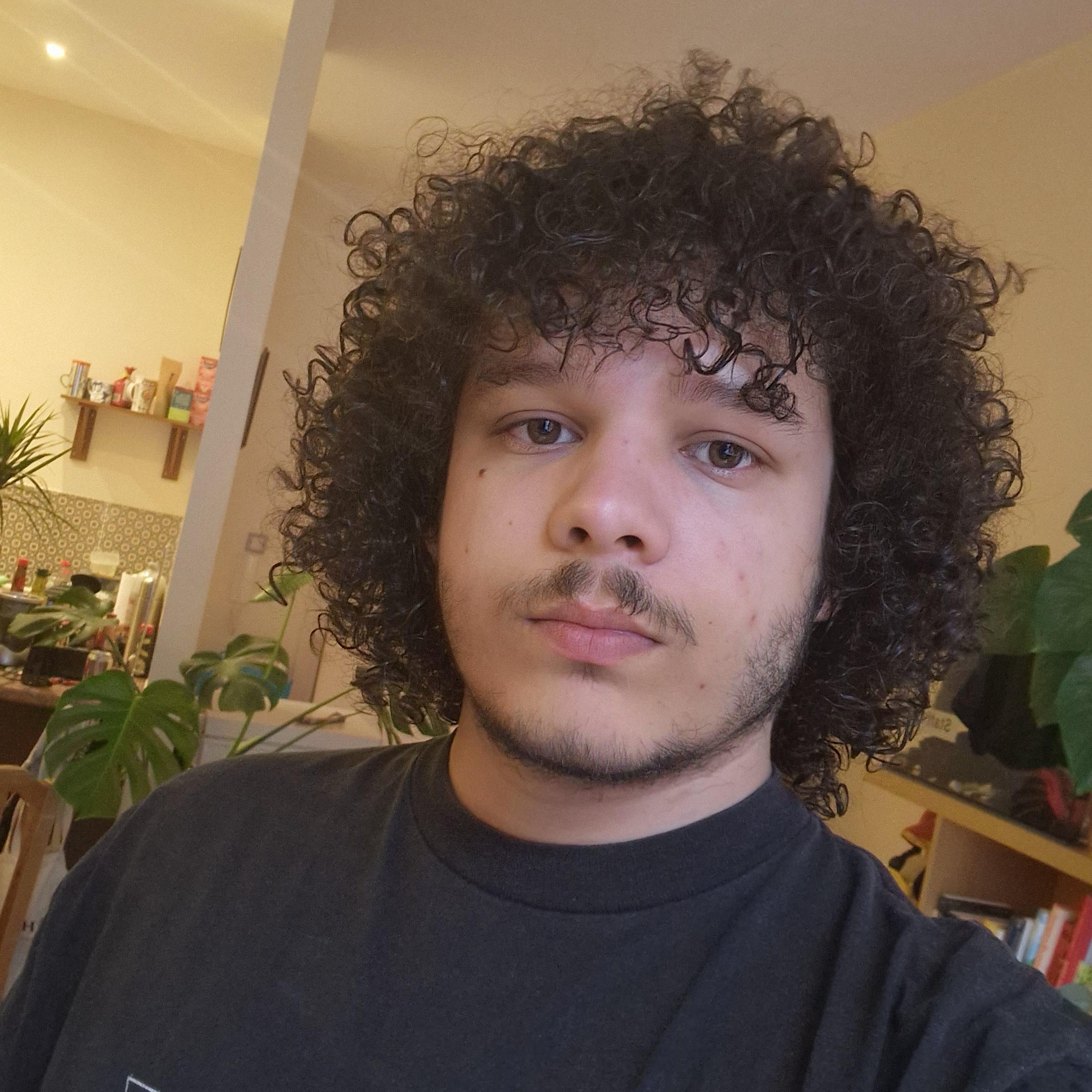 Close-up selfies of a man with dark curly hair wearing a black t-shirt and a green hoodie.