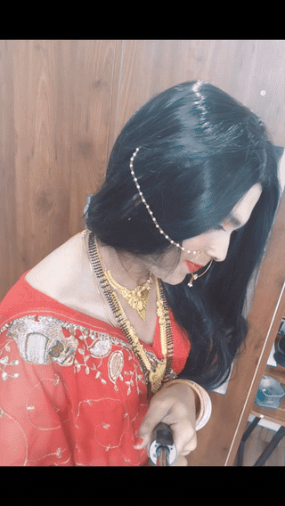 Desi sissy trans woman in a red bridal saree, gold jewelry, and nose ring posing for a video