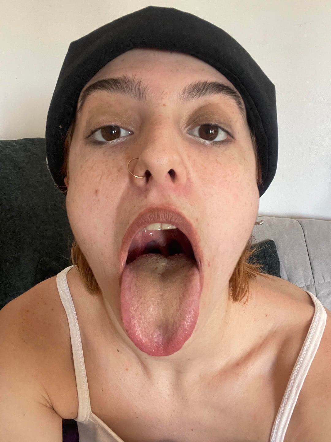 Tomboy woman in a black beanie and white tank top posing for a selfie.