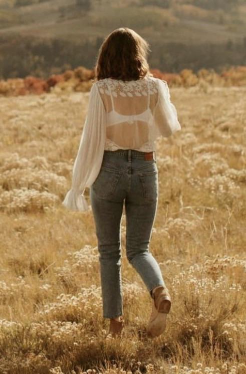 Woman in a white lace blouse and blue jeans embracing a man in an autumn field with mountains.